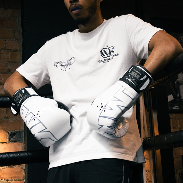 Person in a boxing ring wearing branded gloves and shorts, with a towel in the background.