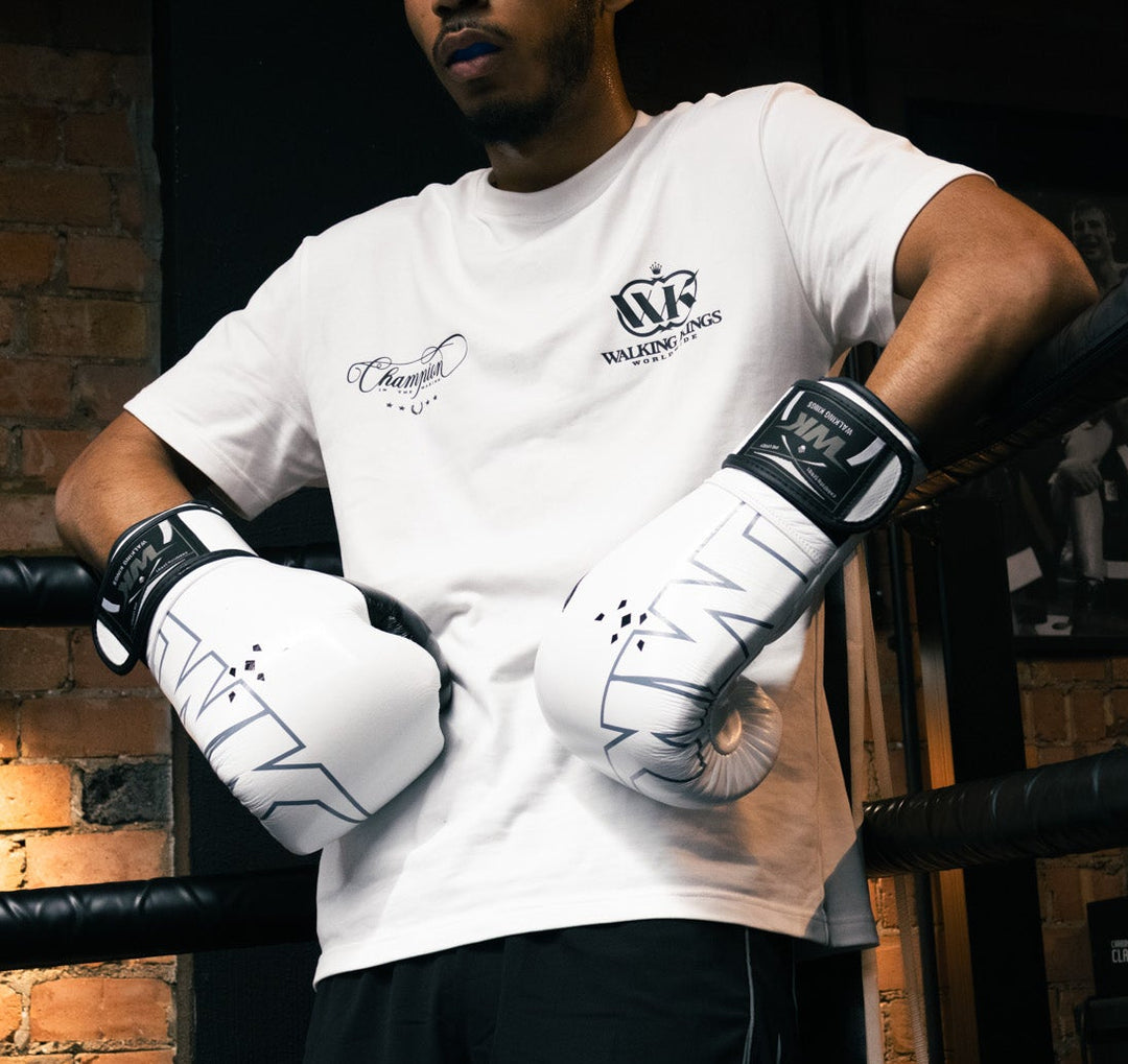 Person in a boxing ring wearing branded gloves and shorts, with a towel in the background.